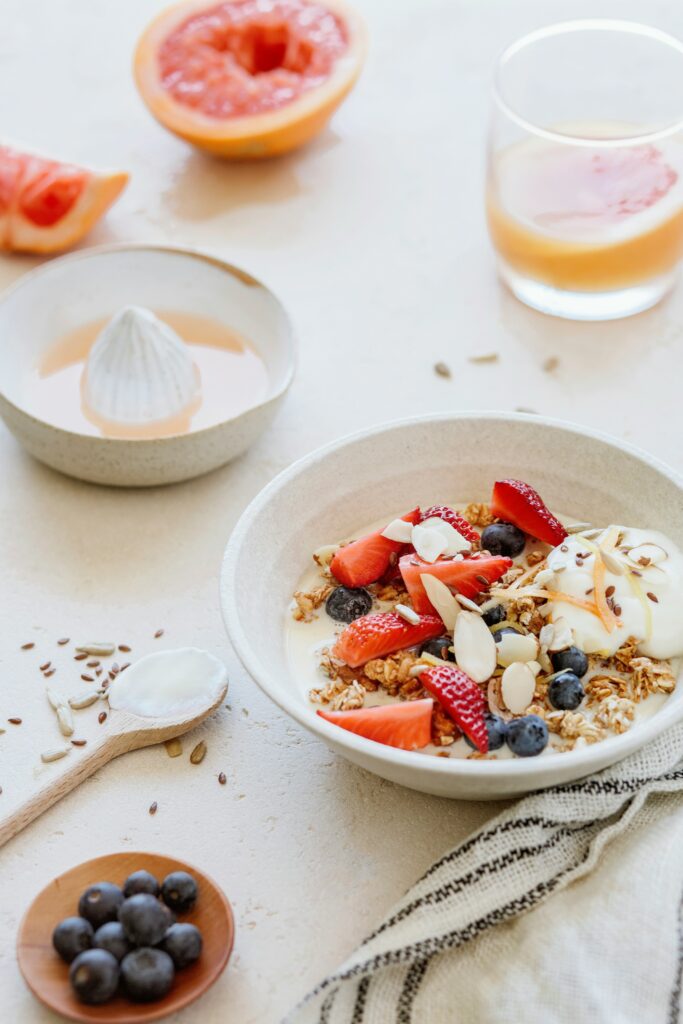 a healthy breakfast scene with a bowl of yogurt with granola and sliced strawberries and almonds and blueberries