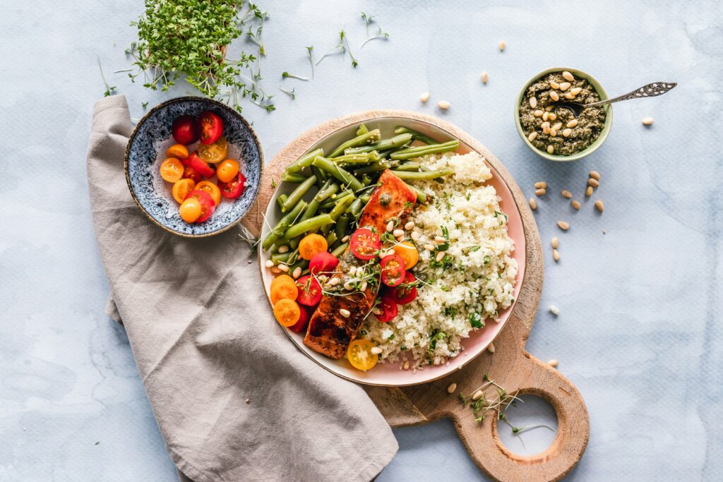 bow of green beans, halved cherry tomatoes, salmon, and grains on a wooden board